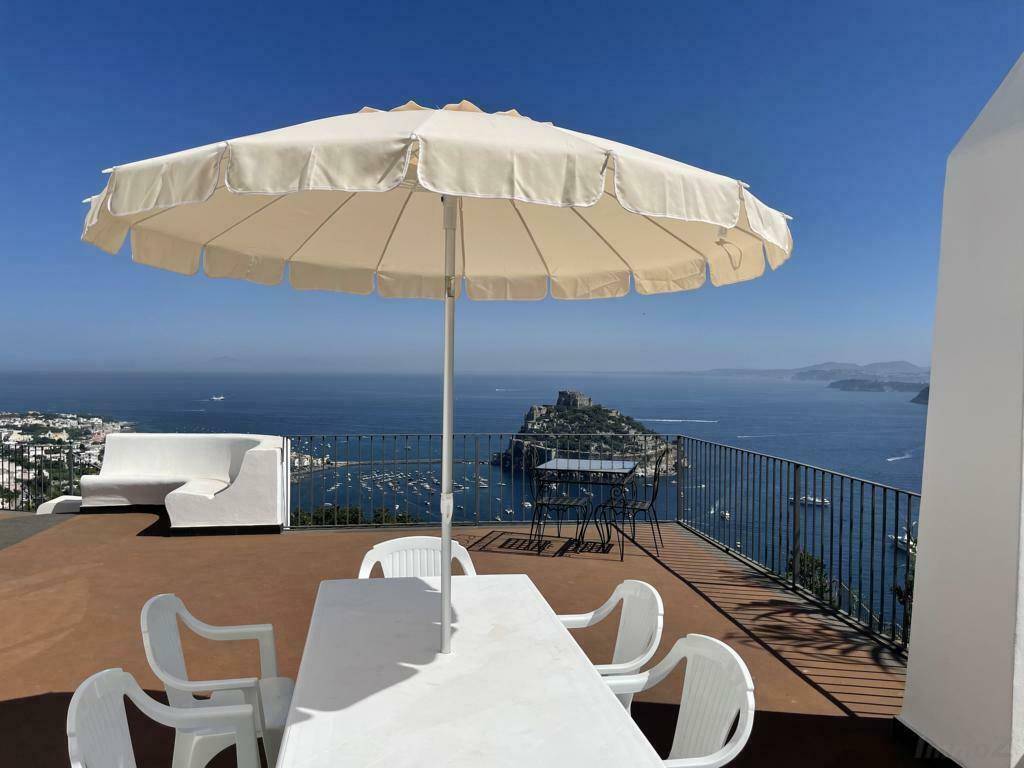 Sonnenterrasse mit großem Sonnenschirm, Esstisch und weitem Blick über das Meer und die Küste.