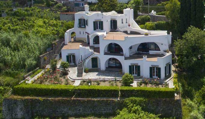 Malerische weiße Villa mit Terrassen und Gärten, eingebettet in grüne Landschaft mit Meerblick.