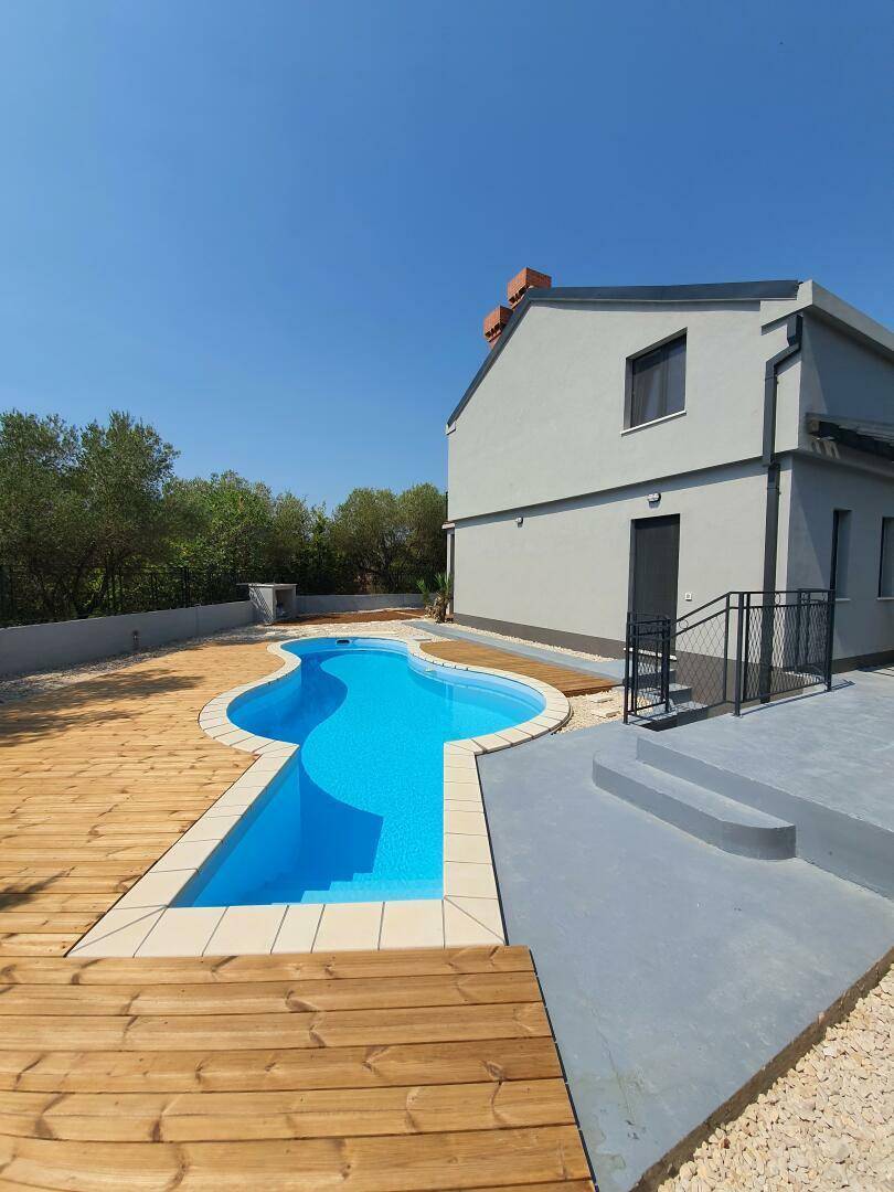 Geschwungener Poolbereich mit Holzdeck und sonniger Umgebung.