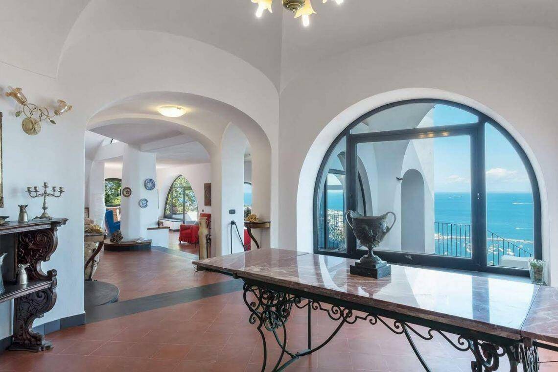Heller Wohnbereich mit Bögen, Terrakottaboden und weitem Meerblick durch große Fenster.