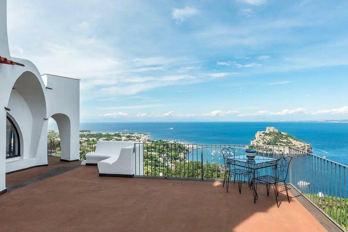 Geräumige Terrasse mit Sitzgelegenheiten und weitem Blick über das Meer und eine Insel.