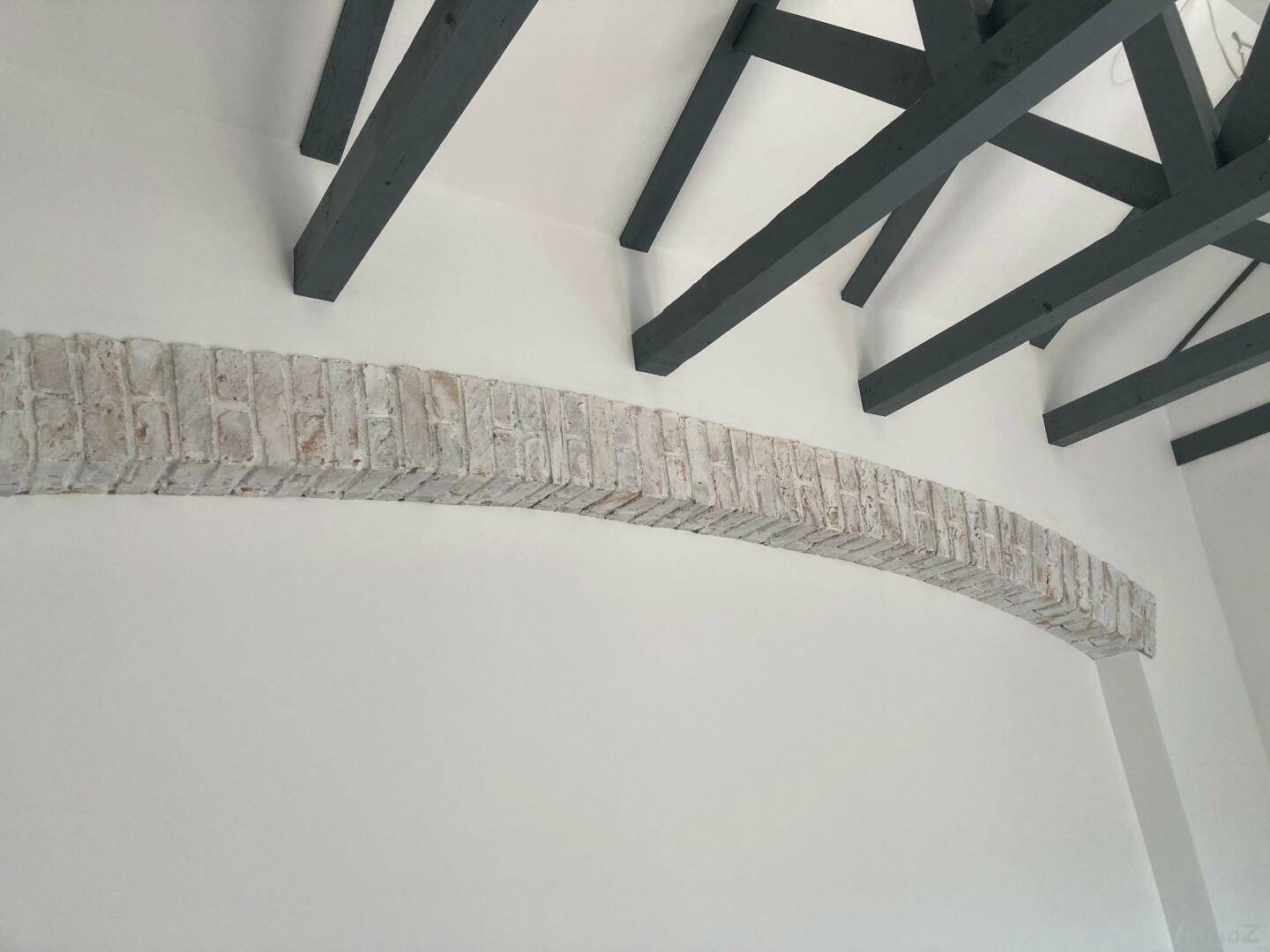 Innenraum mit dekorativem Ziegelbogen und sichtbaren Holzbalken an der Decke.