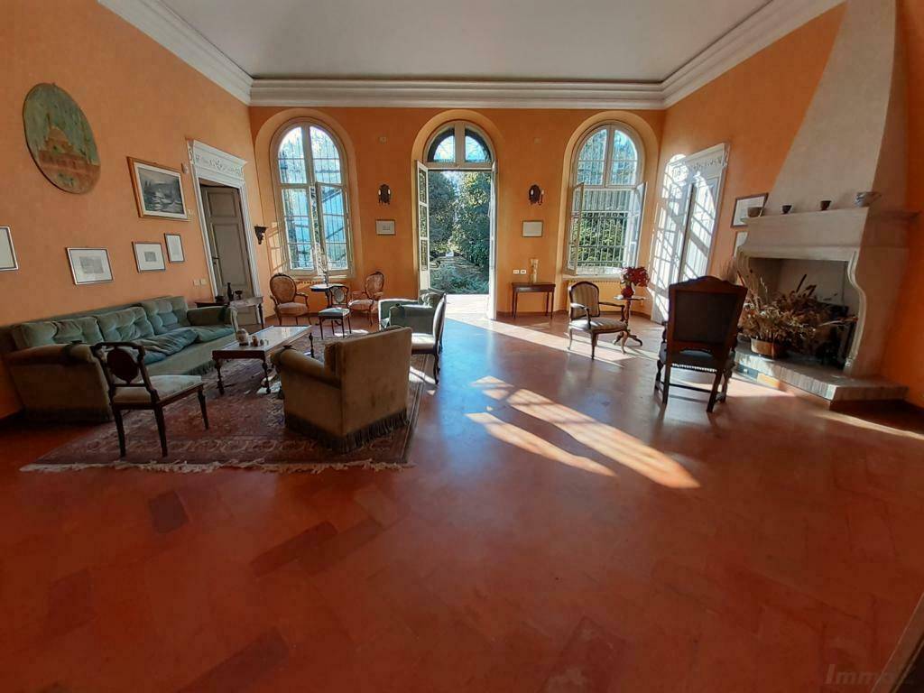 Geräumiges Wohnzimmer mit Kamin, Terrakottaboden und großen Fenstern mit Blick ins Grüne.