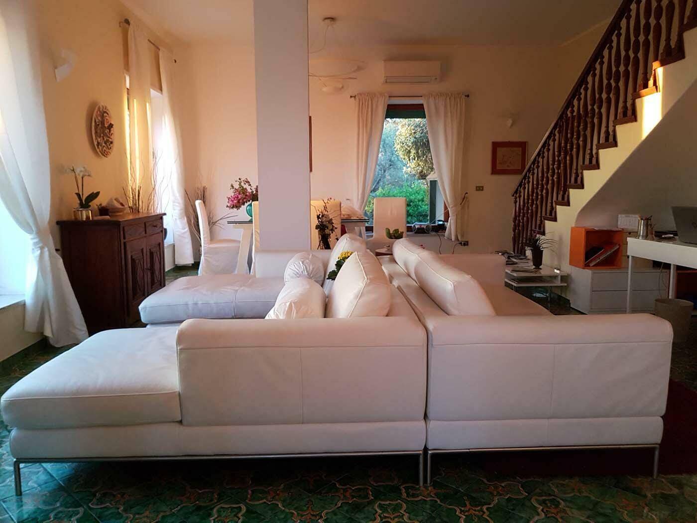 Helles Wohnzimmer mit weißem Sofa, gemusterten Fliesen und einer eleganten Holztreppe.