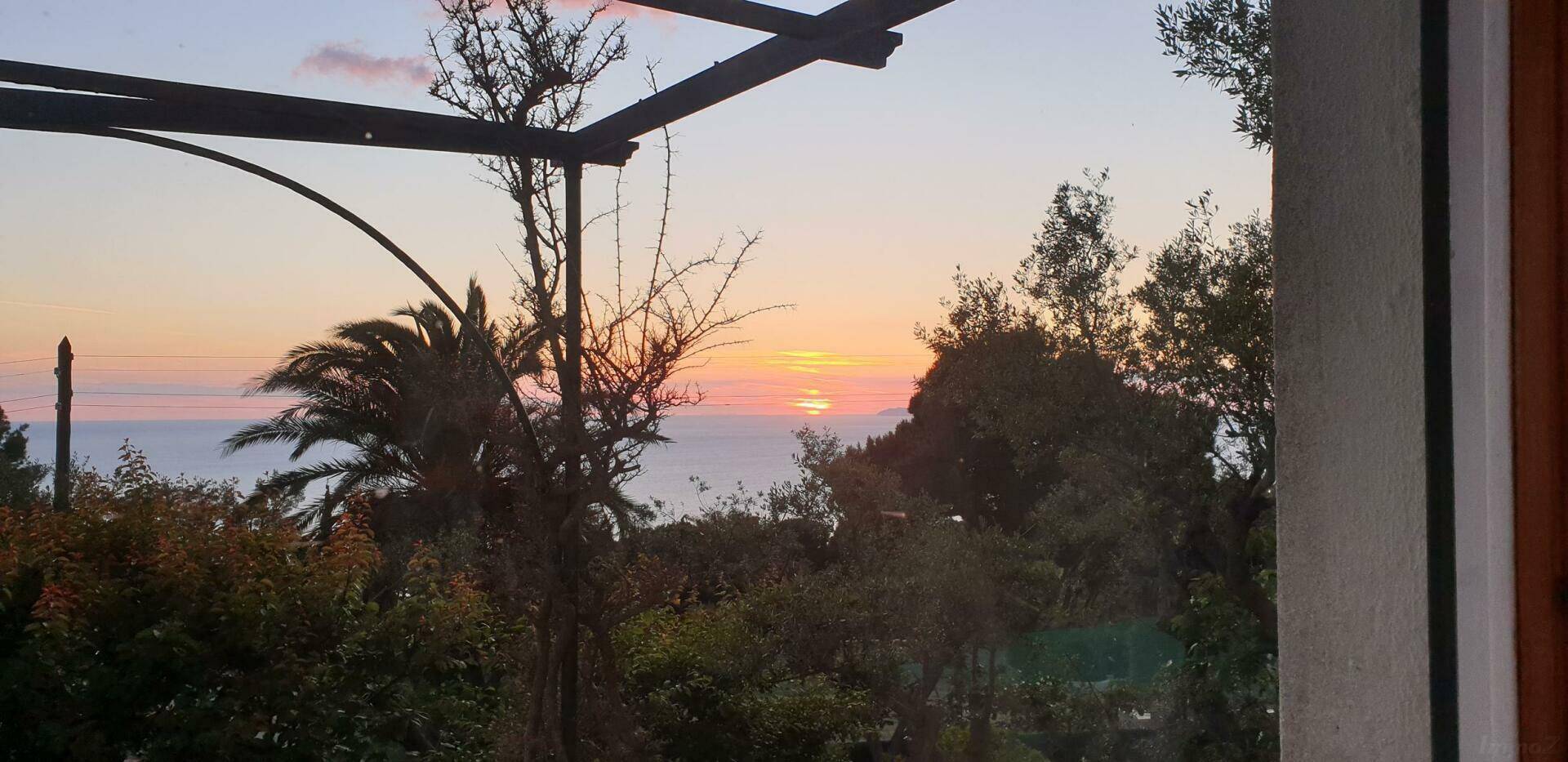 Atemberaubender Sonnenuntergang über dem Meer, eingefangen von einer Terrasse mit Pergola.
