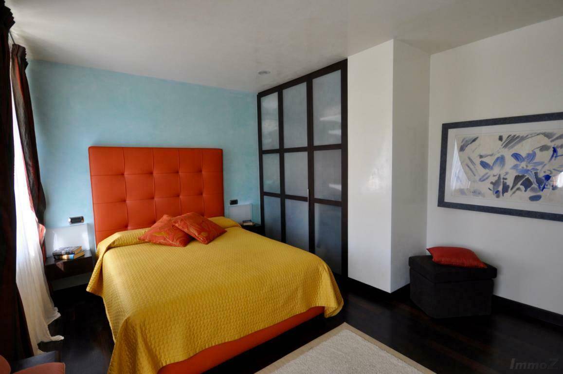 Modernes Schlafzimmer mit orangefarbenem Kopfteil, dunklem Holzboden und blauer Akzentwand.