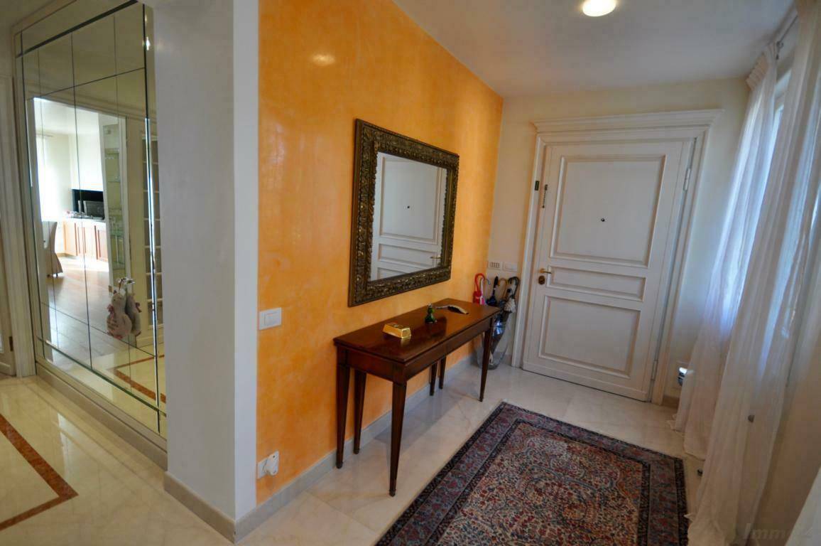 Heller Eingangsbereich mit orangefarbener Akzentwand, Spiegel und elegantem Marmorboden.