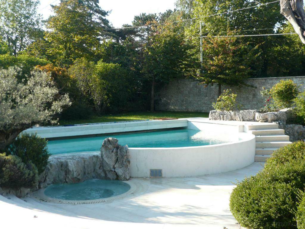 Moderner Poolbereich mit integriertem Whirlpool und Steintreppen in einer grünen Umgebung.