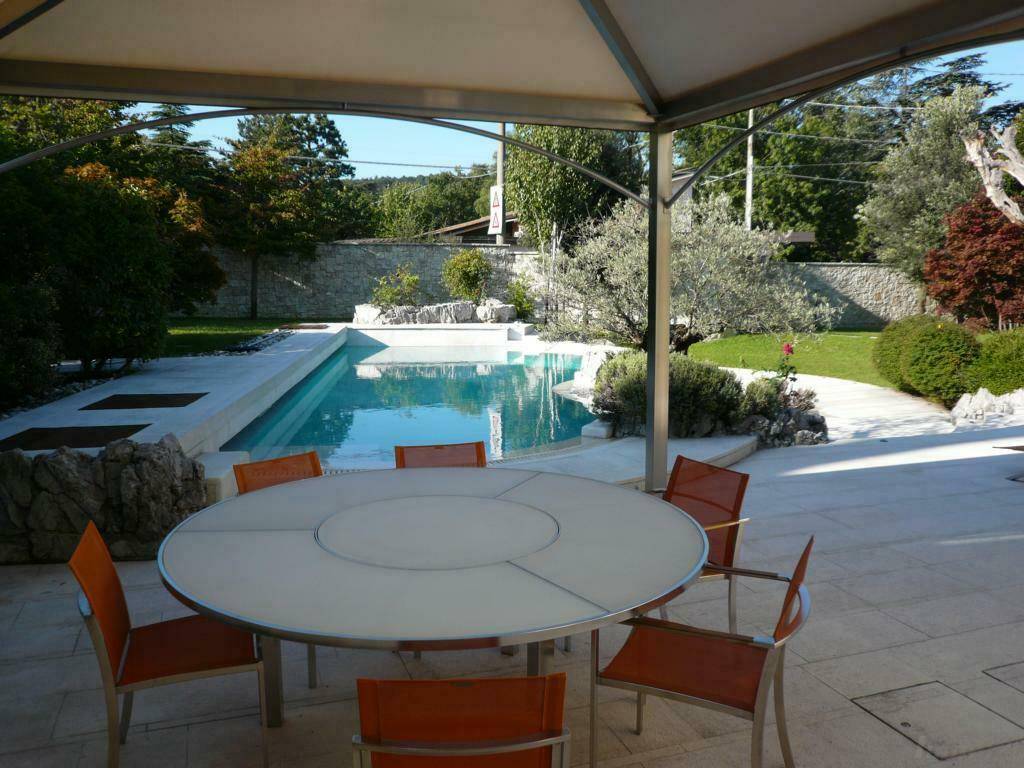 Überdachte Terrasse mit großem Esstisch und Blick auf den Pool und den gepflegten Garten.