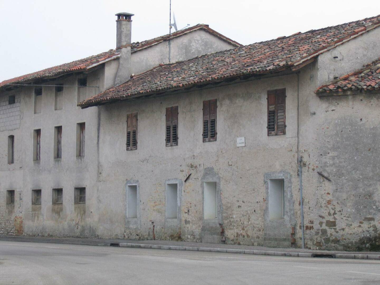 Altes Gebäude mit traditioneller Fassade, kleinen Fenstern und Ziegeldach in ländlicher Umgebung.