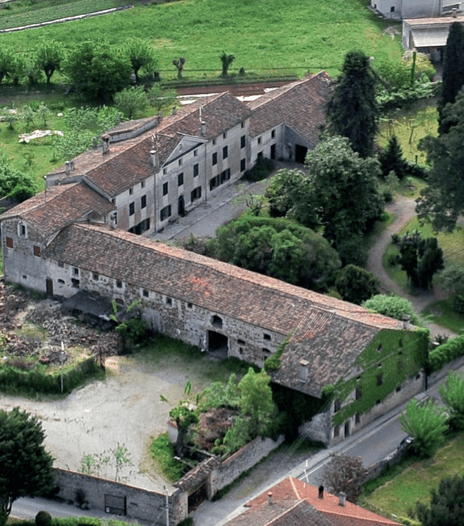 Luftaufnahme eines weitläufigen historischen Anwesens mit mehreren Gebäuden und grünen Flächen.