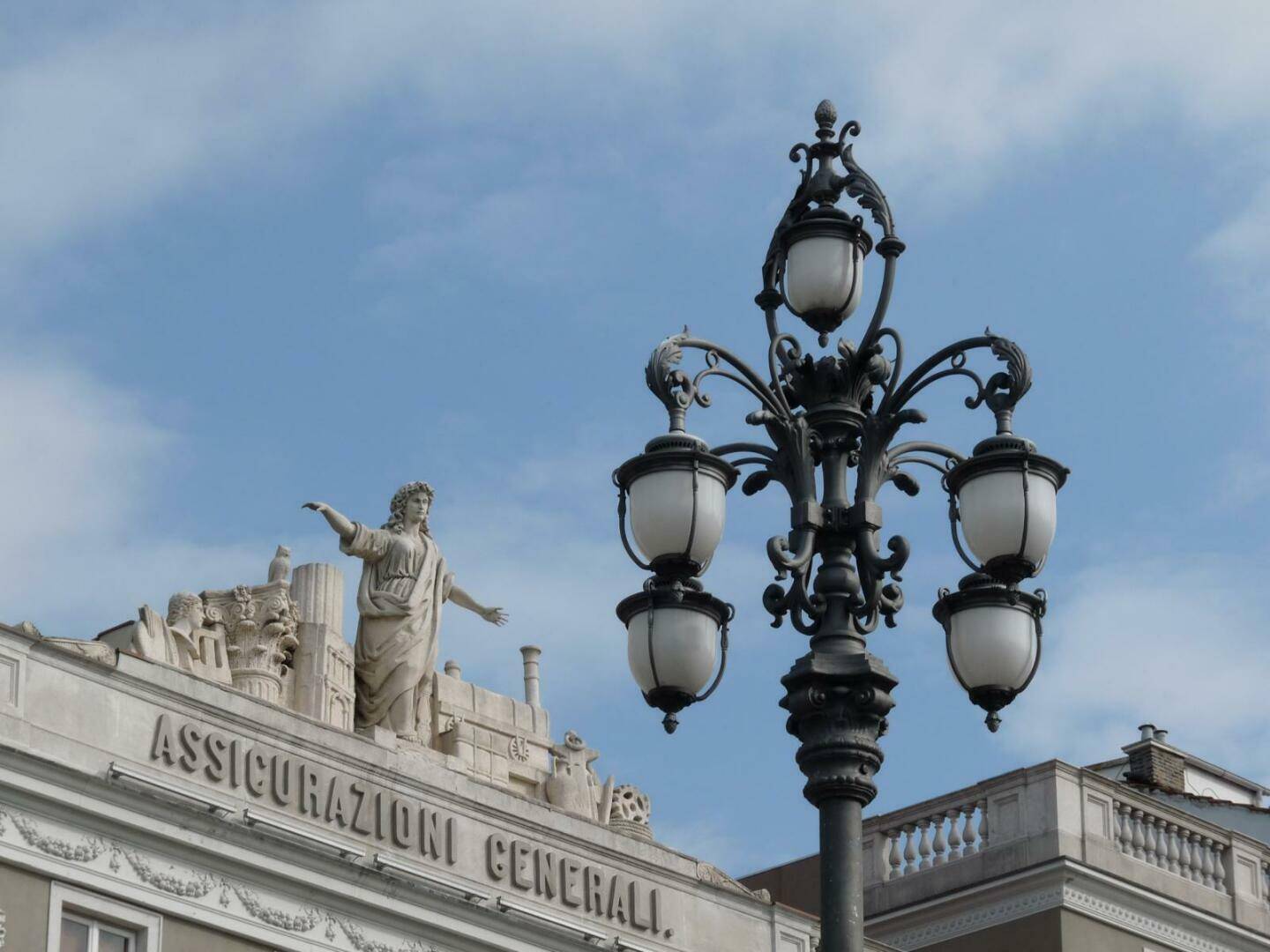 Historische Architektur mit Skulpturen und einer kunstvollen Straßenlaterne unter blauem Himmel.