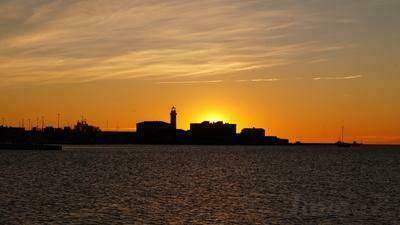 Malerischer Sonnenuntergang über der Silhouette einer Küstenstadt mit ruhigem Meer im Vordergrund.