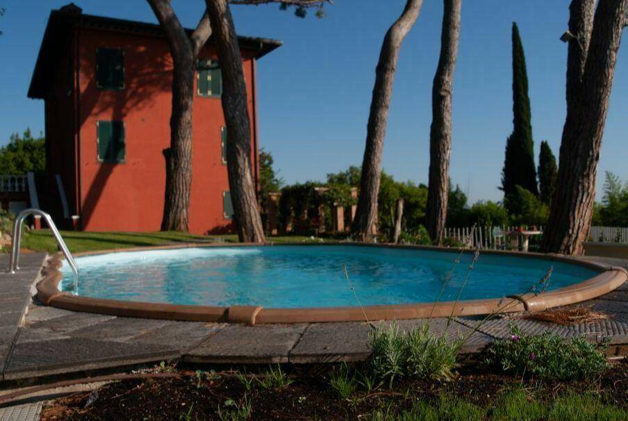 Runder Swimmingpool im Gartenbereich mit hohen Bäumen und dem roten Haus im Hintergrund.