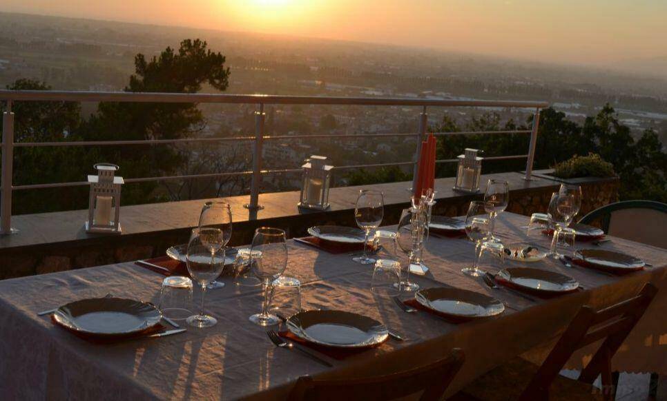 Festlich gedeckter Esstisch auf einer Terrasse mit atemberaubendem Sonnenuntergang und Fernblick.