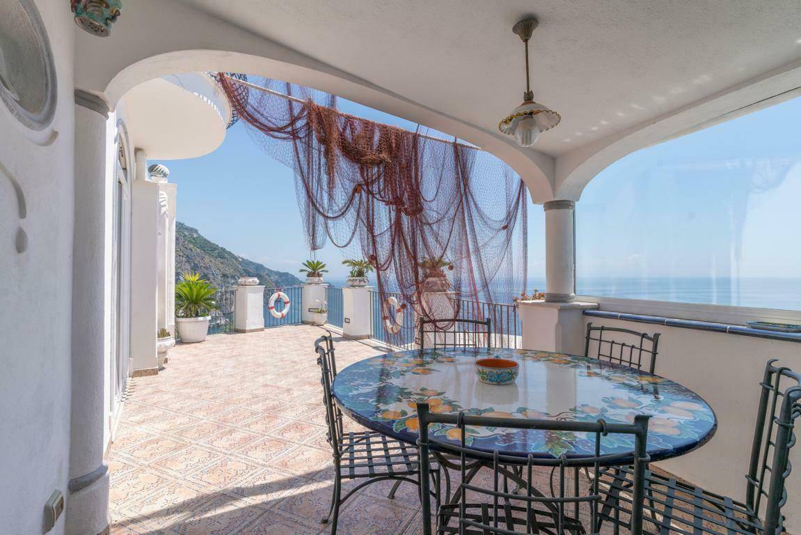 Überdachter Balkon mit Meerblick, Esstisch und dekorativem Fischernetz.
