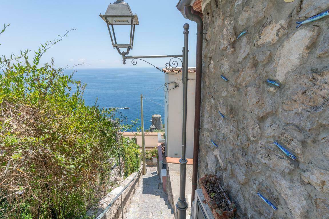 Steiler Weg mit Steinmauer und Laterne, der zum Meer hinunterführt.