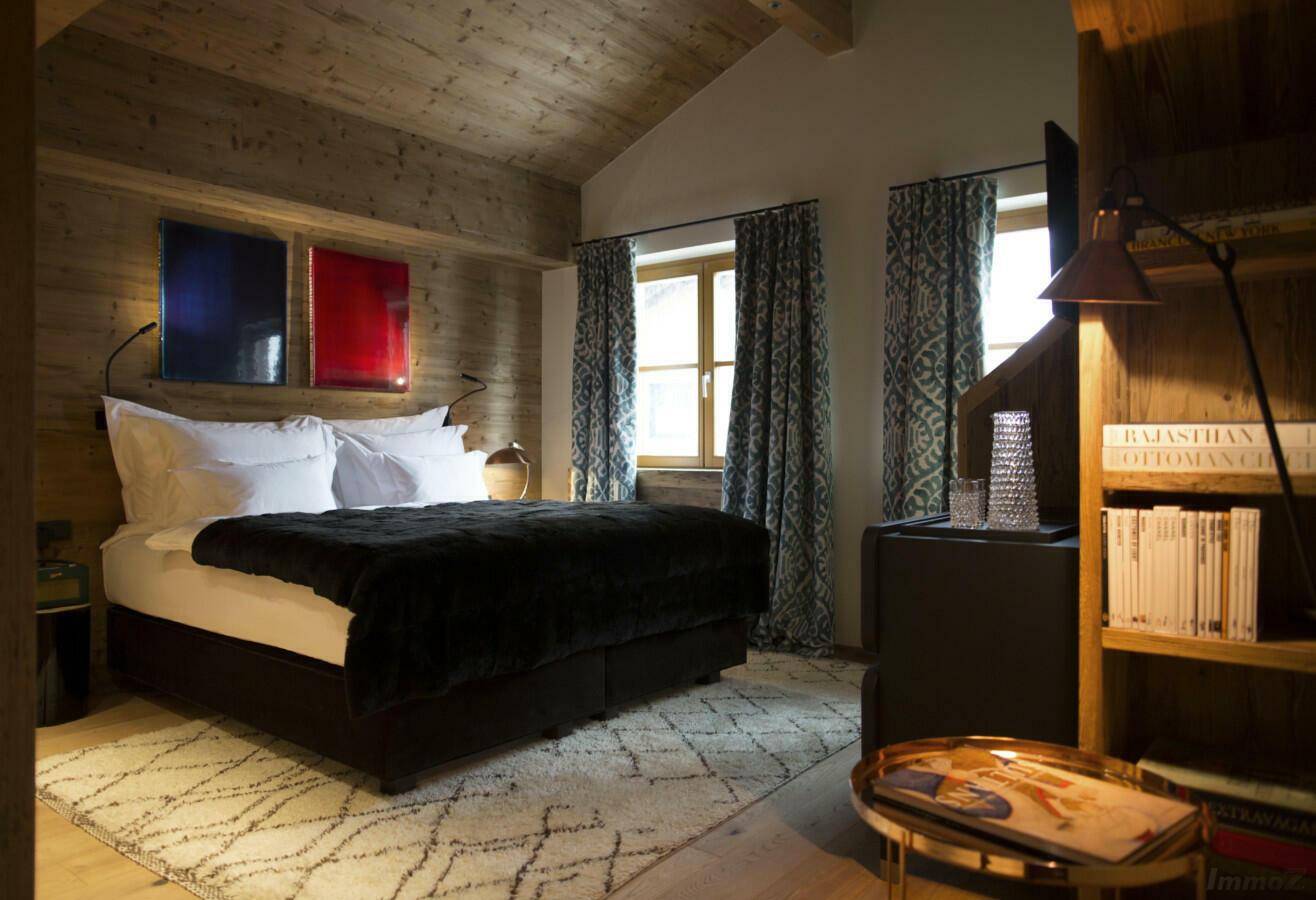 Gemütliches Schlafzimmer im alpinen Stil mit Holzwänden, großem Bett und schrägen Decken.