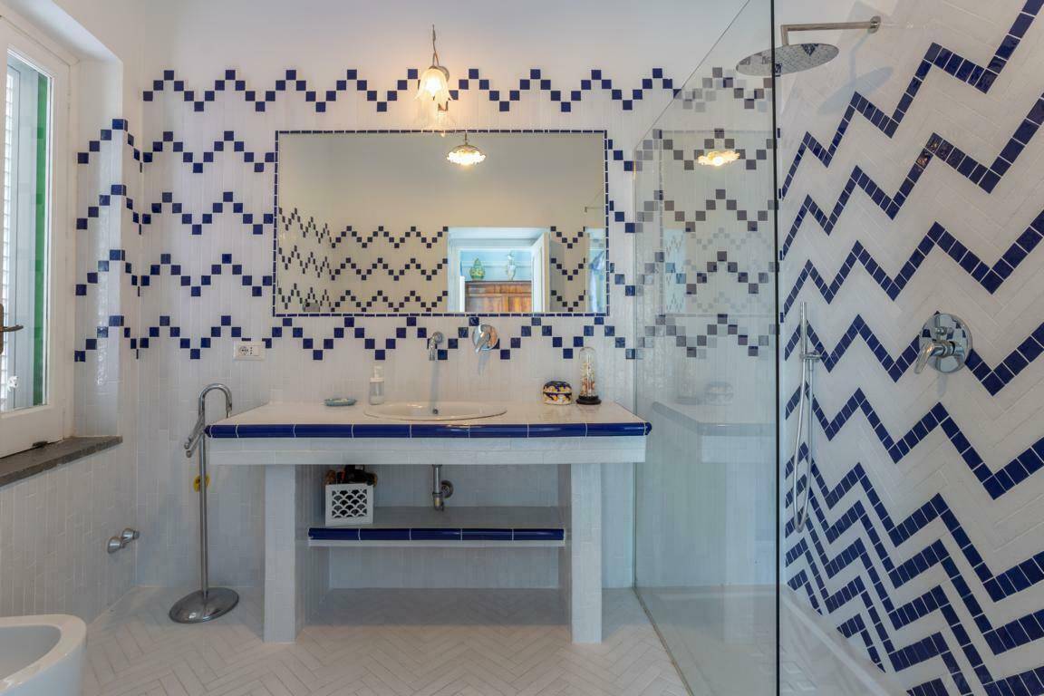 Modernes Badezimmer mit auffälligen blau-weißen Zickzack-Fliesen und einer geräumigen Duschkabine.