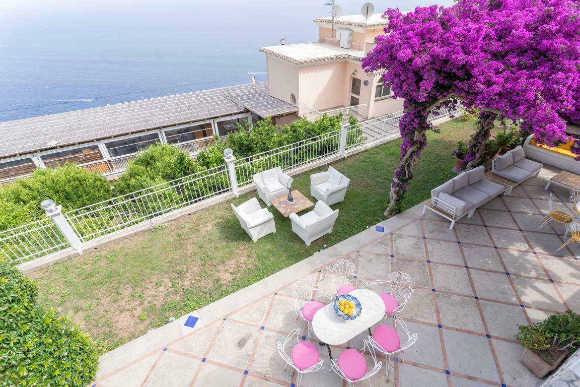 Weitläufige Terrasse mit verschiedenen Sitzbereichen, Rasenfläche und blühenden Bougainvillea mit Meerblick.
