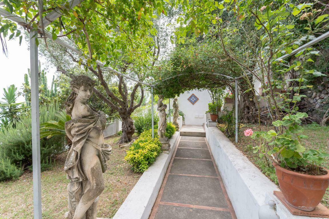 Malerischer Gartenweg, gesäumt von Statuen und üppiger Vegetation, führt durch das Anwesen.