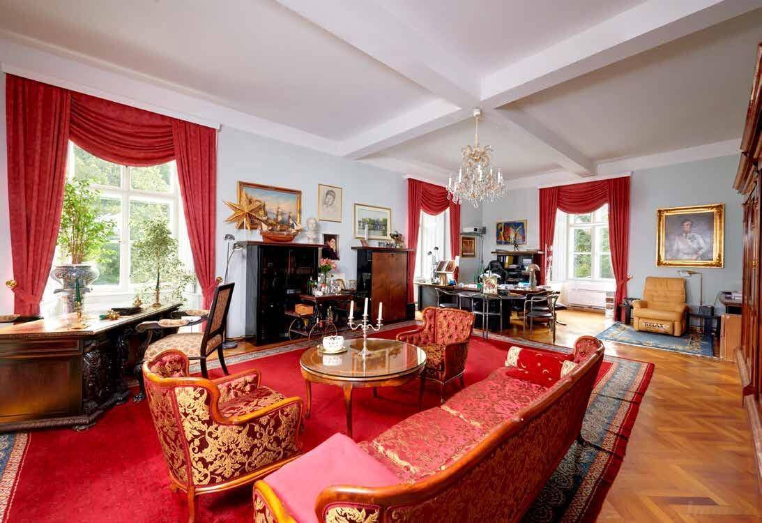 Geräumiges Wohnzimmer mit rotem Teppich, eleganten Möbeln und großen Fenstern.