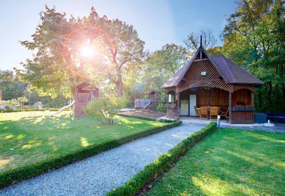 Weitläufiger Gartenbereich mit Spielplatz, Holzpavillon und sonnigen Rasenflächen.