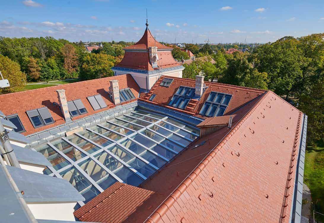 Dachlandschaft des historischen Gebäudes mit roten Ziegeln und modernen Glasdachkonstruktionen.