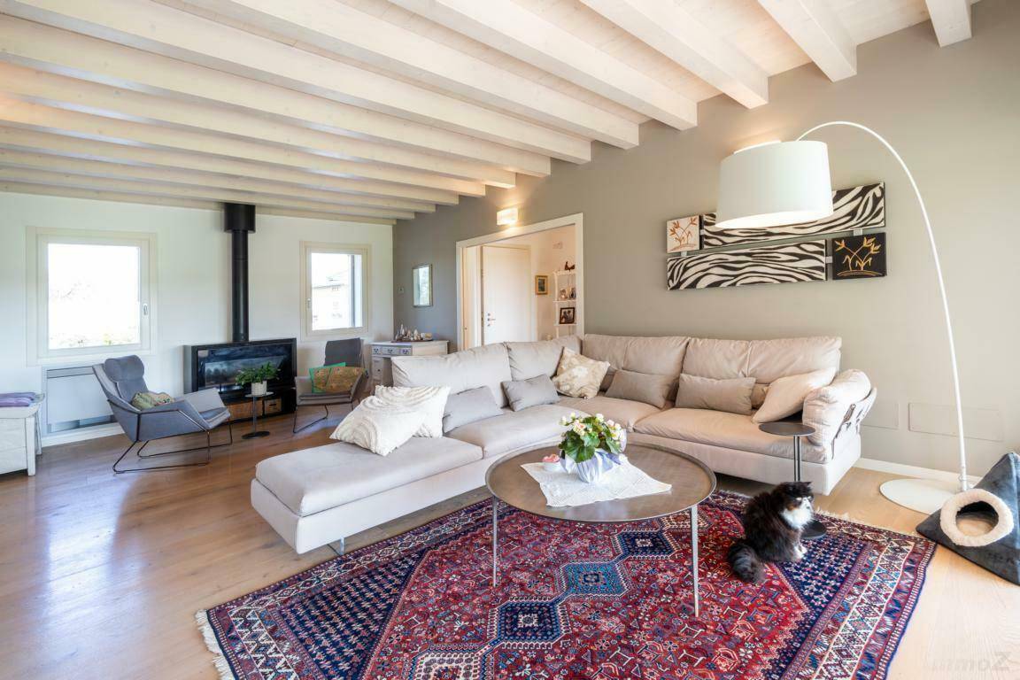 Geräumiger Wohnbereich mit großem Sofa, Kamin und Holzboden unter sichtbaren Deckenbalken.