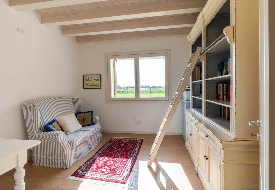 Gemütliches Arbeitszimmer mit großem Bücherregal, Holzboden und Blick ins Grüne.
