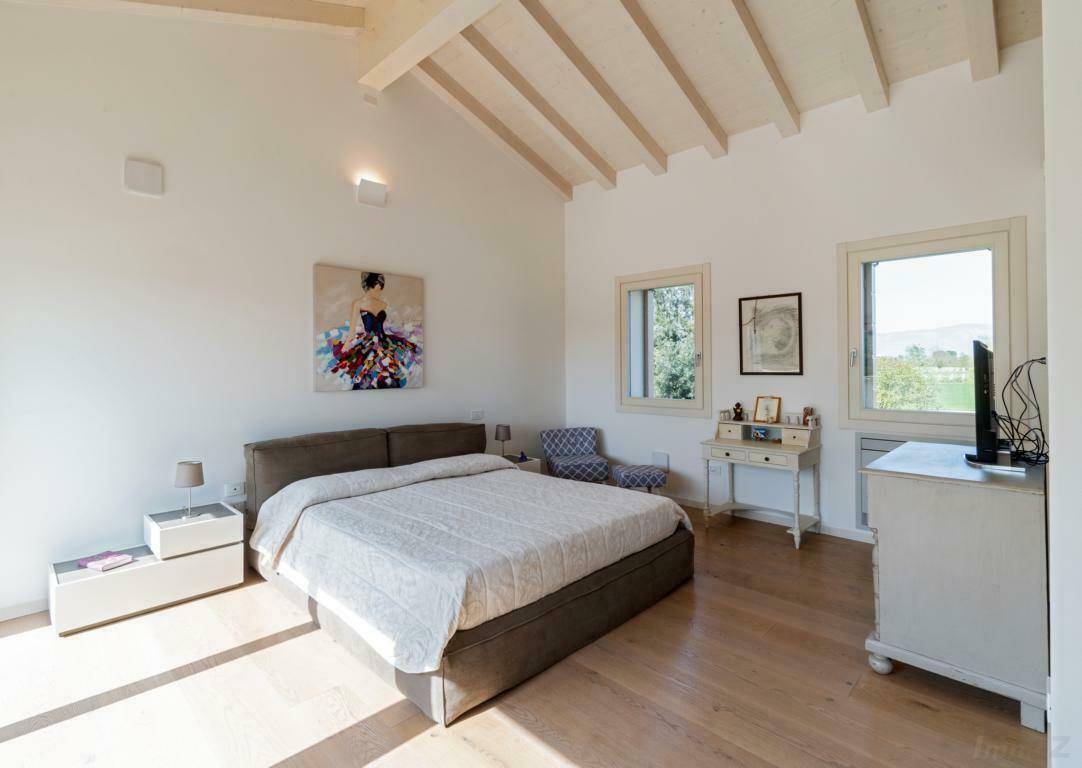 Helles Schlafzimmer mit Holzboden, sichtbaren Deckenbalken und großen Fenstern mit Weitblick.