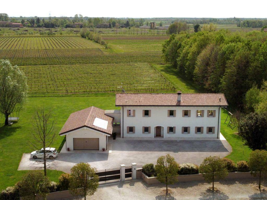 Weitläufige Ansicht des Hauses mit Garage, umgeben von grünen Feldern und Weinbergen.