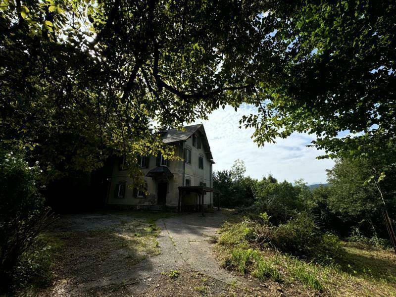 Historisches Gebäude, umgeben von dichtem Baumbestand, mit Blick auf die hügelige Landschaft.