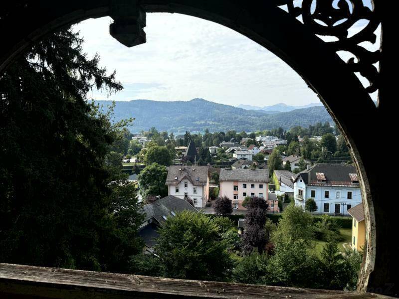 Panoramablick auf die umliegende Ortschaft und die bewaldeten Berge durch ein verziertes Fenster.