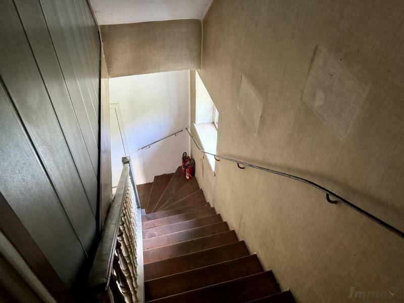Holztreppe mit Geländer in einem Flur, der natürliches Licht durch ein kleines Fenster erhält.
