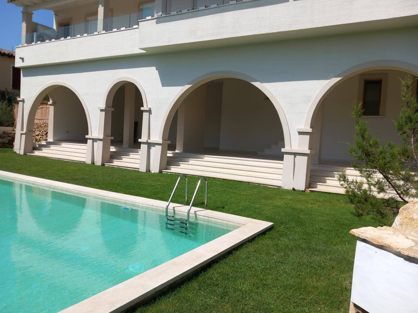 Elegante Gebäudefassade mit markanten Bögen und einem gepflegten Swimmingpool auf einer grünen Rasenfläche.