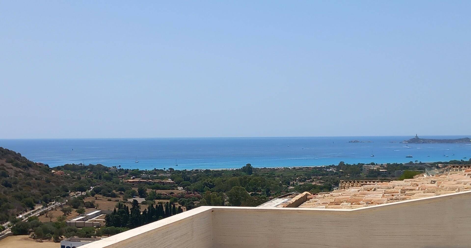 Weitläufiger Blick auf das tiefblaue Meer, die Küste und die grüne Landschaft von einer erhöhten Terrasse.