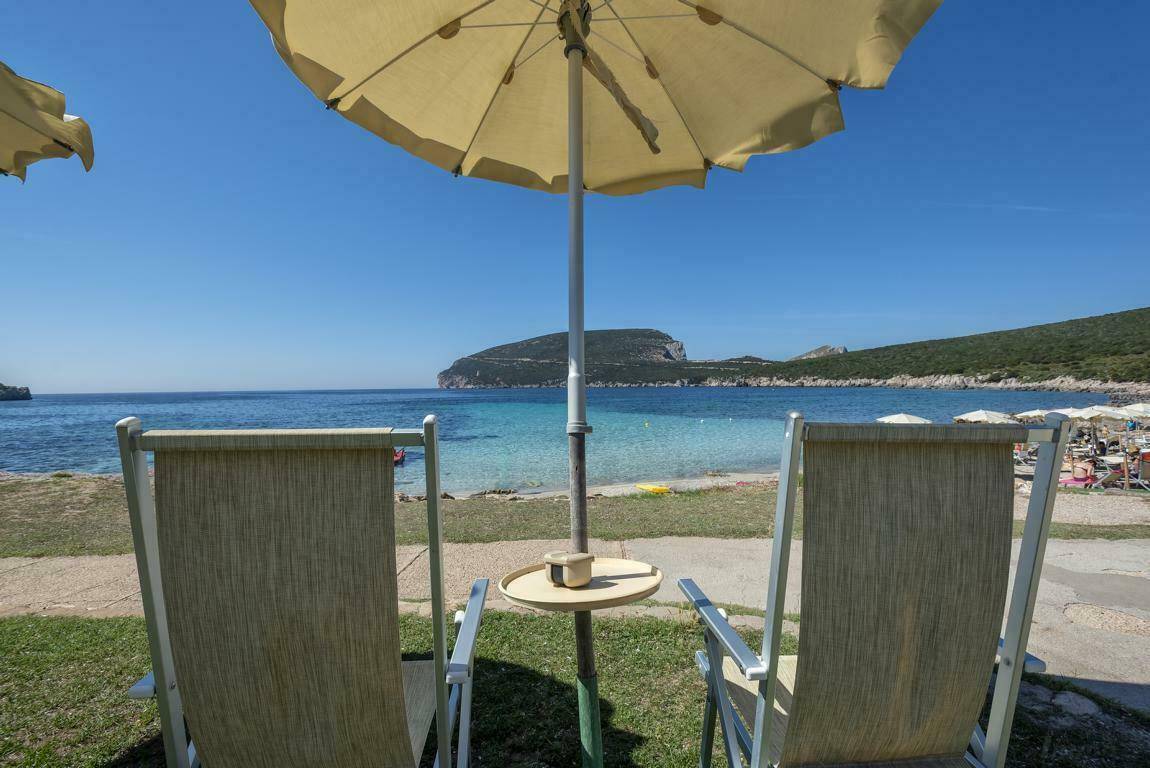 Zwei Liegestühle auf einer Rasenfläche mit Sonnenschirm und weitem Blick auf das blaue Meer.