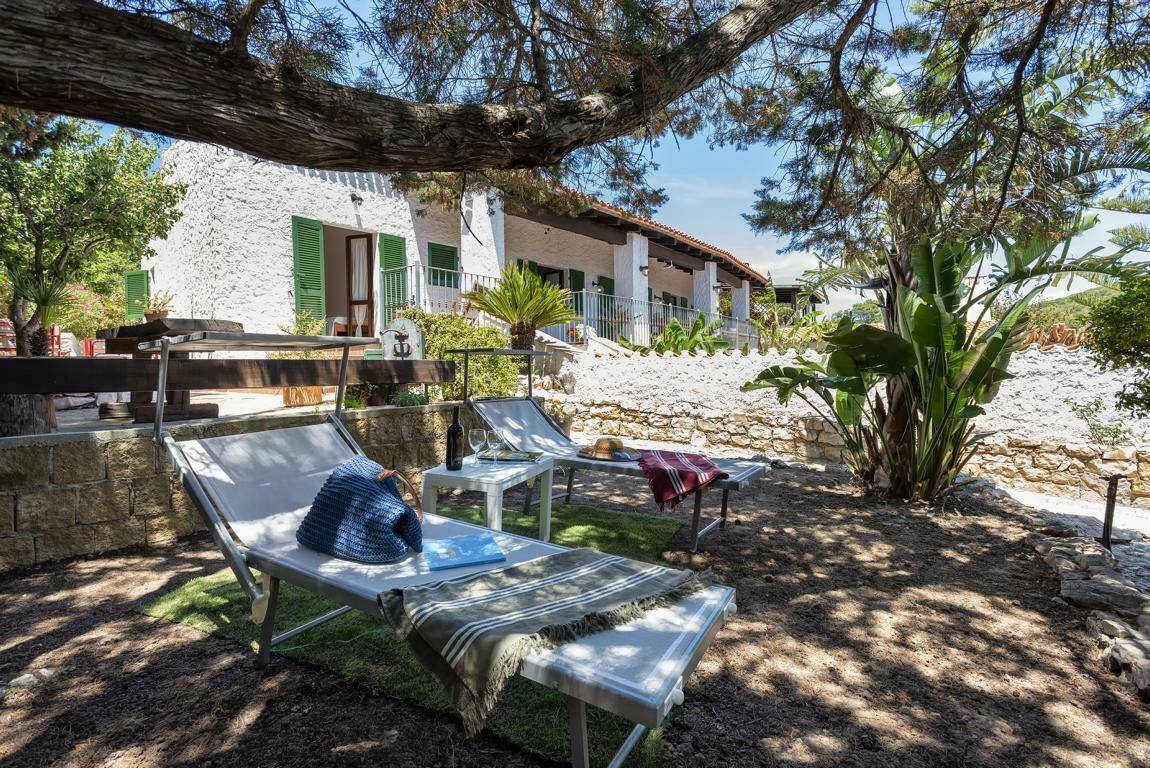 Entspannender Gartenbereich mit Liegestühlen unter schattenspendenden Bäumen vor dem Haus.