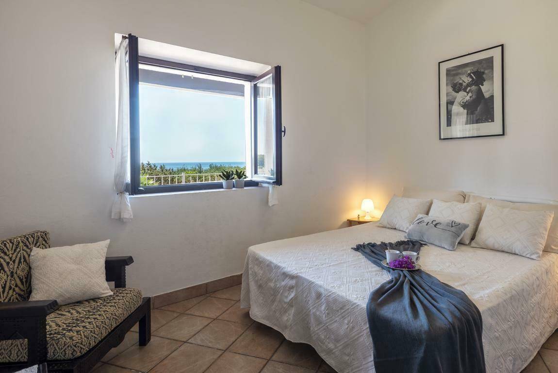 Helles Schlafzimmer mit Doppelbett, Sessel und Fenster mit Blick auf das Meer und die Natur.