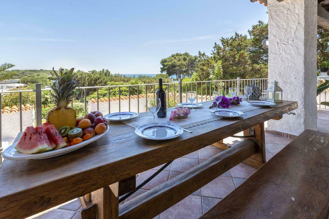 Großer Holztisch auf der Terrasse, gedeckt für ein Essen im Freien mit Meerblick im Hintergrund.