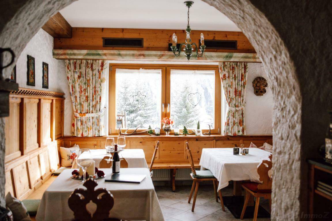 Rustikaler Essbereich mit Holzbänken, Tischen und einem großen Fenster, das den Blick auf die verschneite Landschaft freigibt.