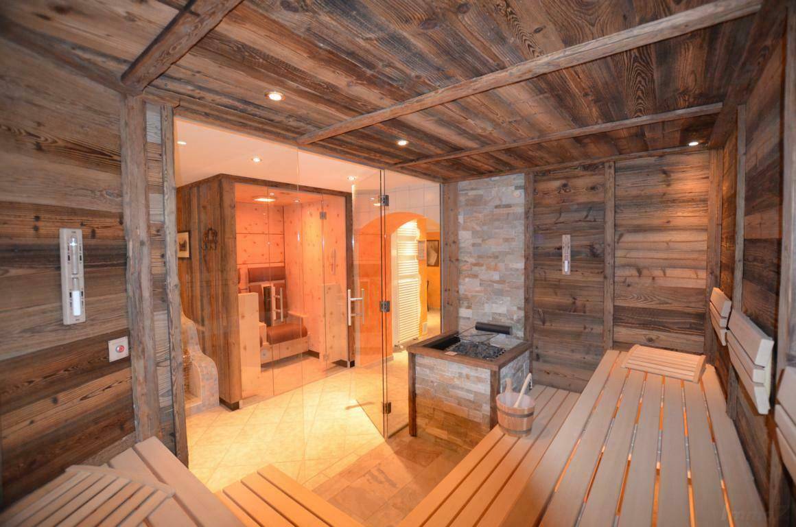 Moderne Sauna mit Holzbänken und Steinwand, angrenzend an eine Duschkabine mit Glaswänden.