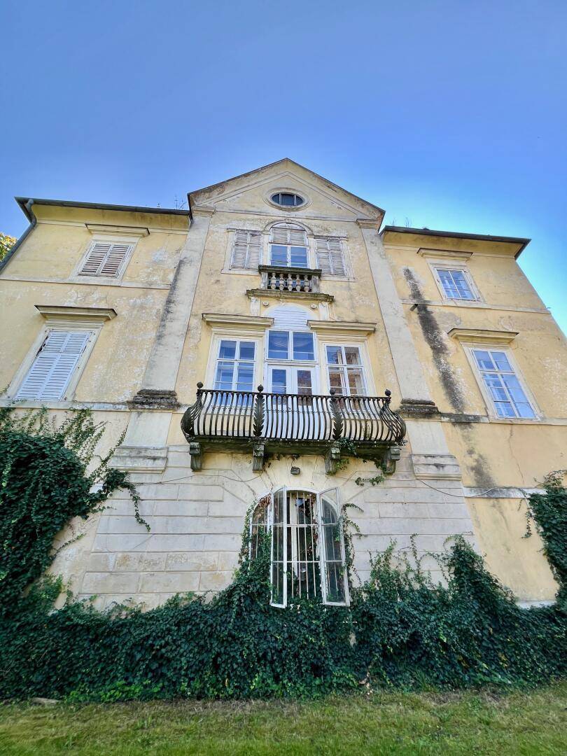 Ansicht der historischen Villa von unten mit verwitterter Fassade und bewachsenen Mauern.