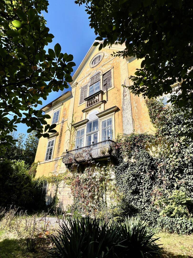 Historische Villa mit gelber Fassade, umgeben von dichtem Grün und Kletterpflanzen.