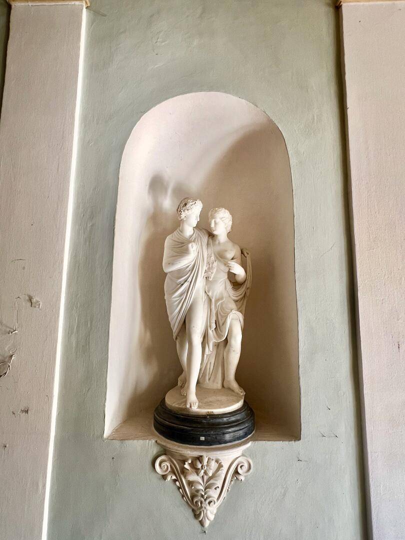Marmorstatue in einer Wandnische, umgeben von hellgrünen Wänden und Stuckverzierungen.