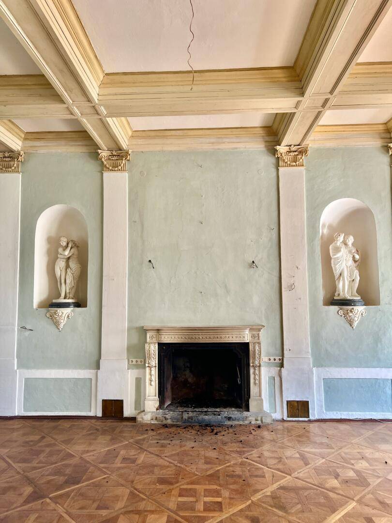 Geräumiger Saal mit Kamin, Wandnischen und Parkettboden, bereit zur Renovierung.