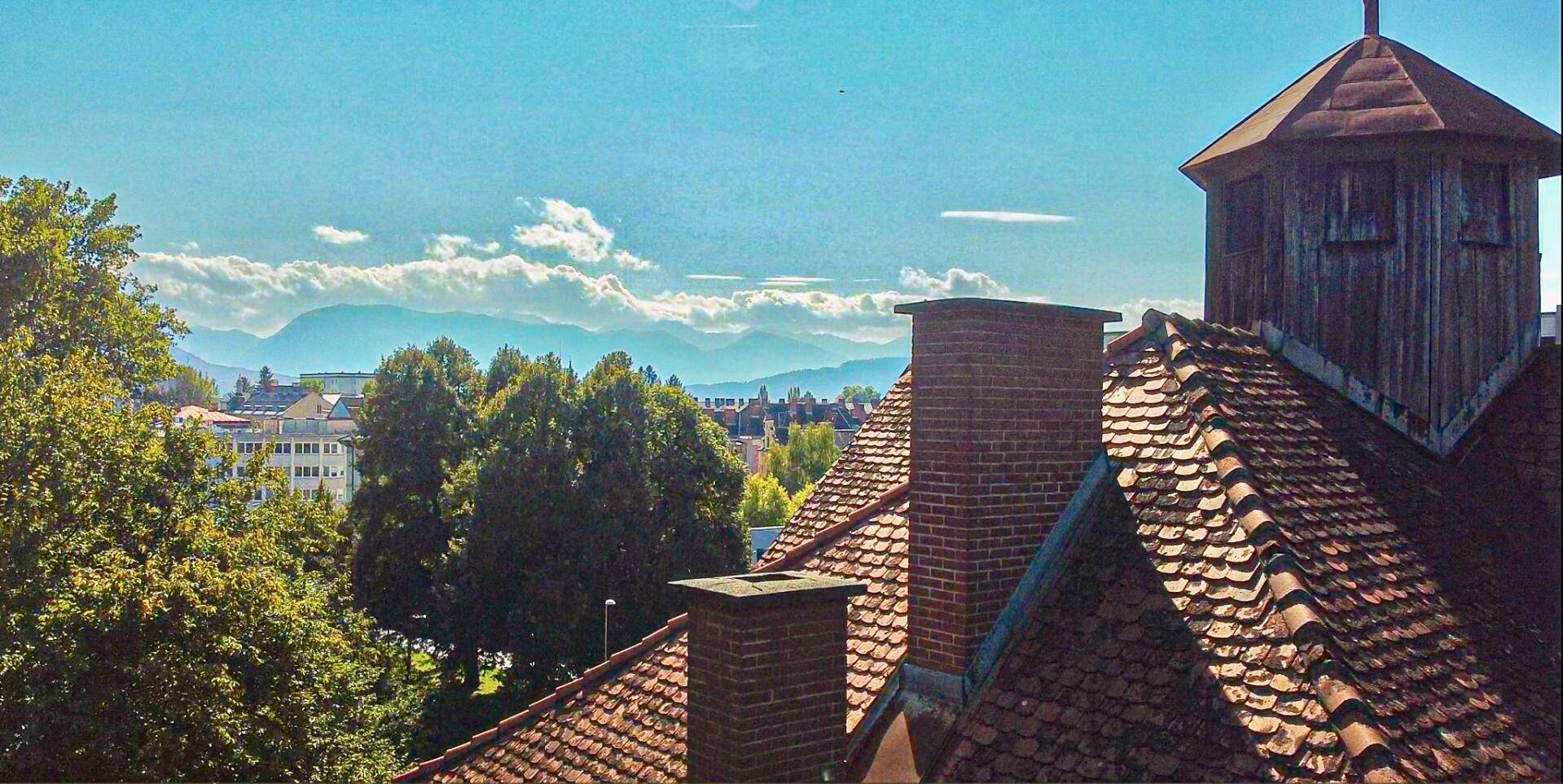 Blick über die Ziegeldächer der Villa auf die umliegende Stadt und ferne Berge.