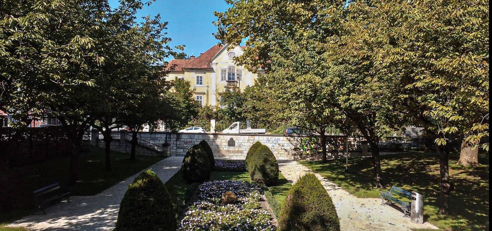 Gepflegter Park mit Bänken und Bäumen, im Hintergrund die historische Villa.