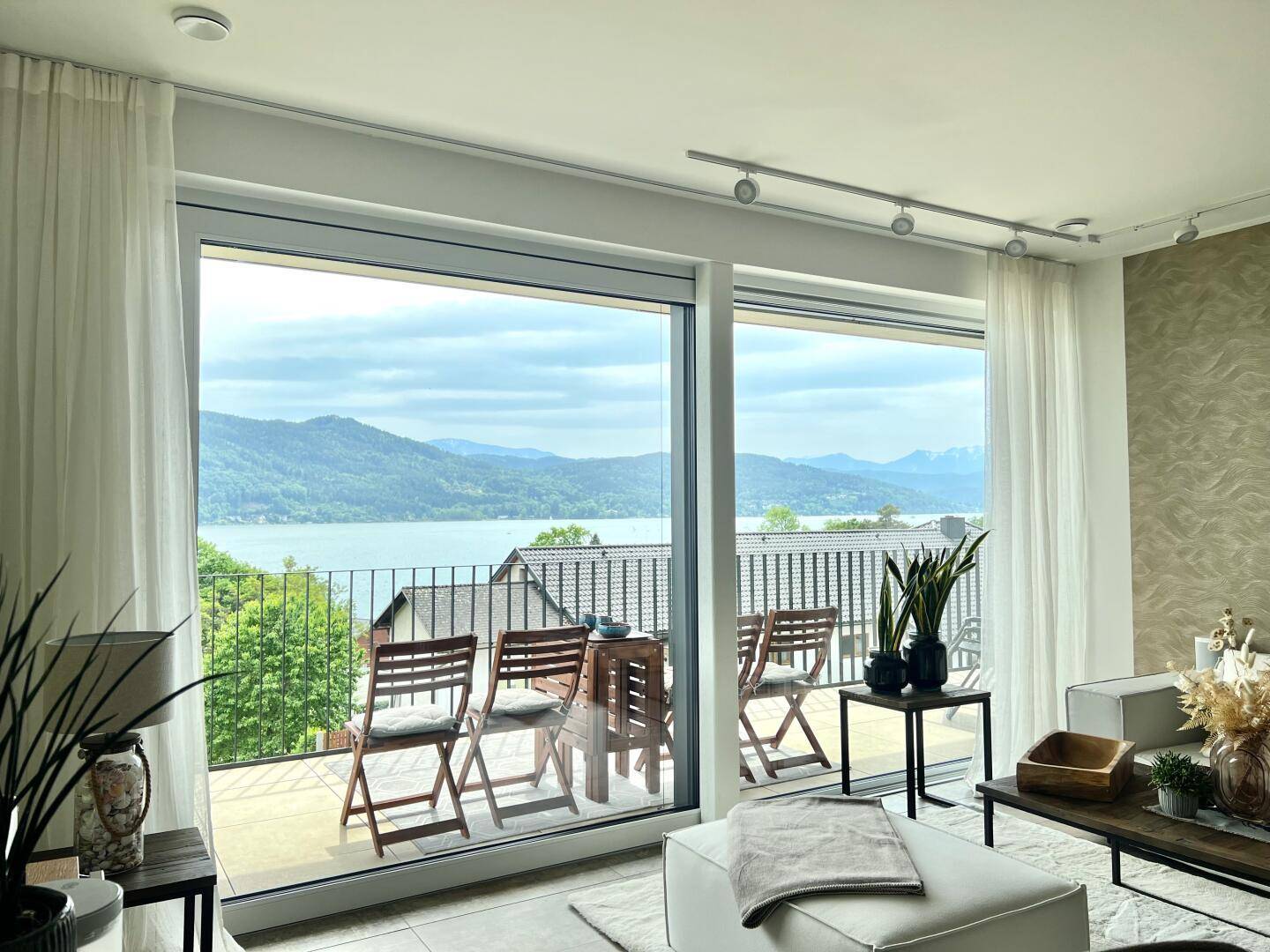 Lichtdurchflutetes Wohnzimmer mit raumhohen Fenstern und einem atemberaubenden See- und Bergblick.